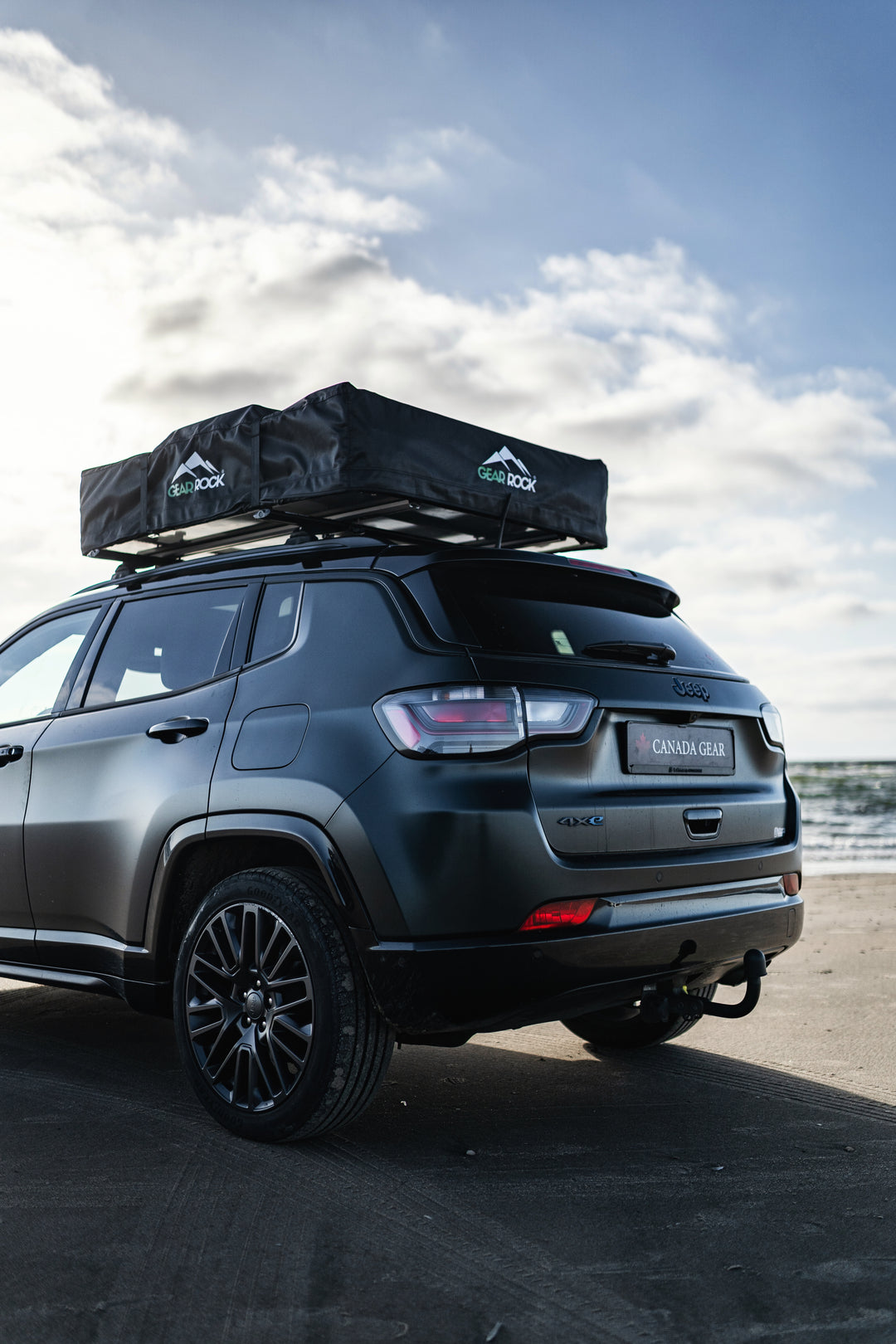 Jeep mit geschlossenem Dachzelt von Gear Rock steht am Strand bei windigem Wetter.